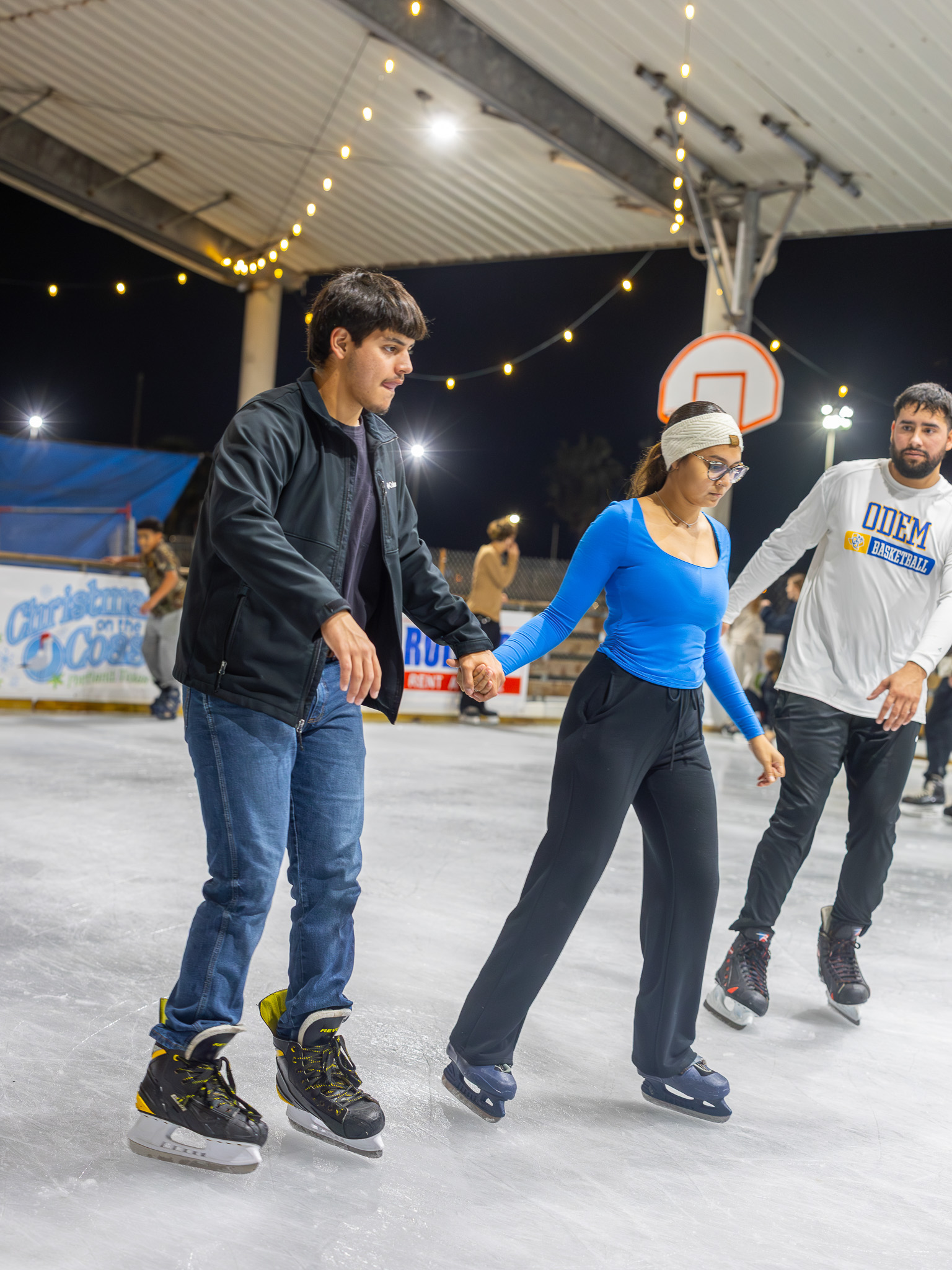 Friends ice skating together under string lights