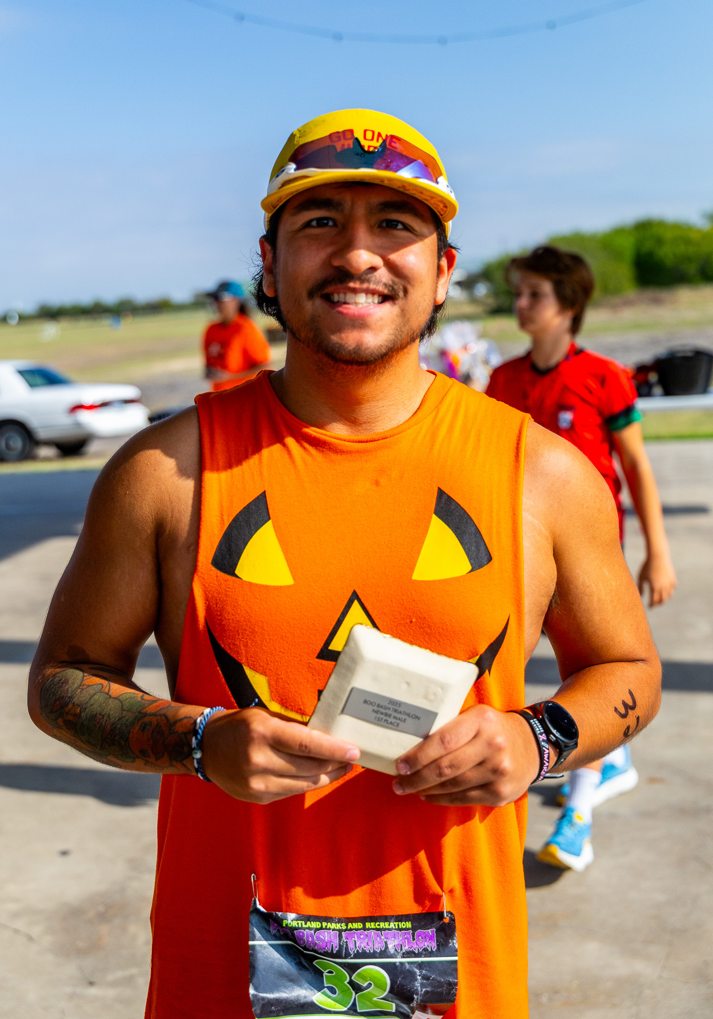 A finisher in a jack-o&rsquo;-lantern tank top holding his award