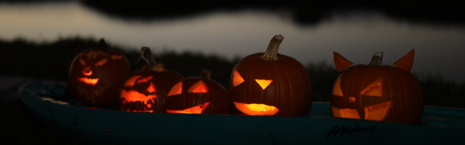 A row of glowing carved jack-o&rsquo;-lanterns at dusk