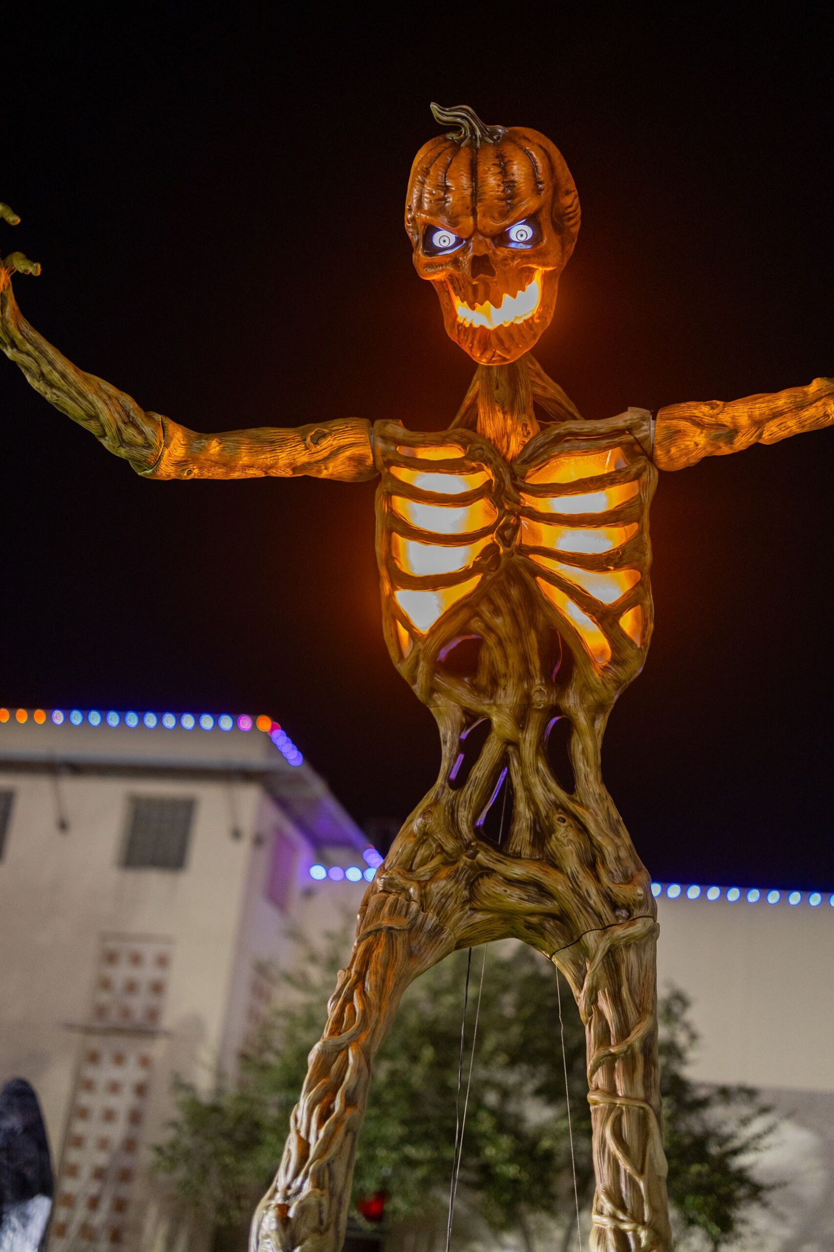 A giant glowing pumpkin-head skeleton at night